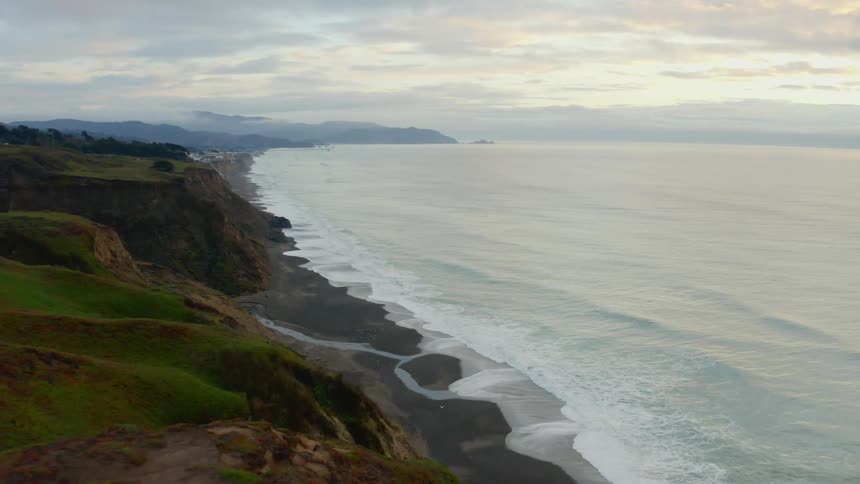 Ocean waves come to a cliff lined shore with black sand beaches