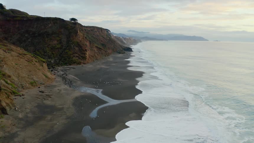 Waves crashing on the sandy beach near cliffs