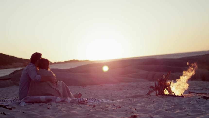 A man and woman hold each other by a crackling fire a sunset