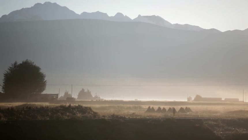 A man rides a bike down a dusty road in front of some mountains