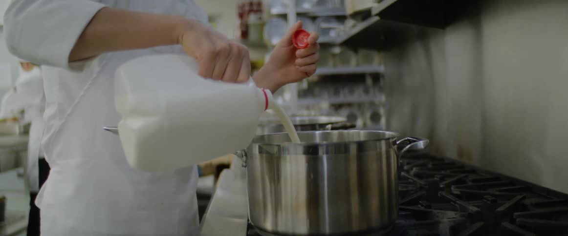 Chef pouring milk into large pot in a restaurant kitchen