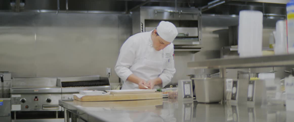 A chef in a restaurant kitchen spoons cooked greens onto a platter