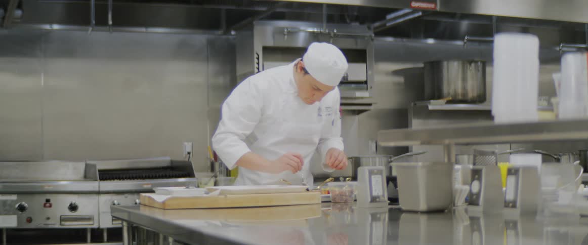 A chef adds ingredients to a plate of food in a commercial kitchen