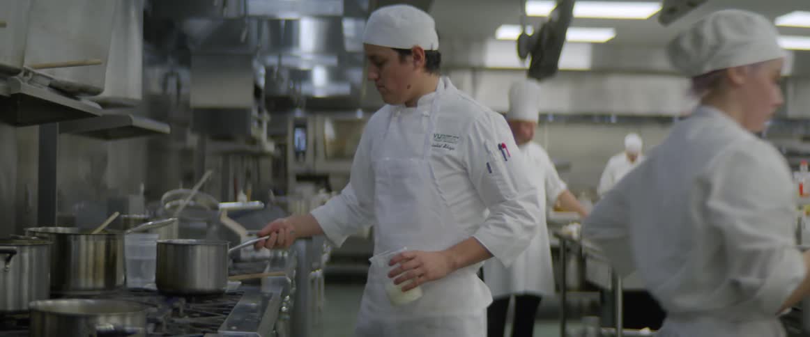 Multiple chefs work in a kitchen while cooking