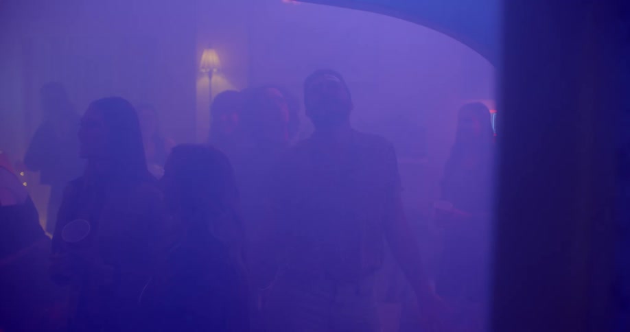 A man dances inside of a club filled with people and purple lighting
