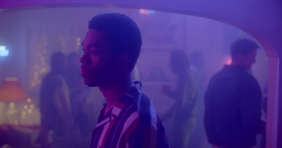 A group of teens talk and dance in smokey room