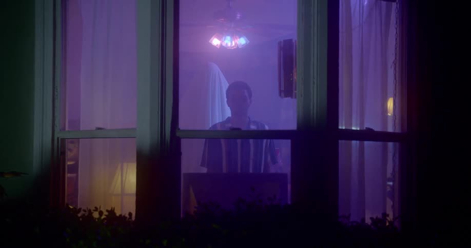 A person stands by a window with purple light