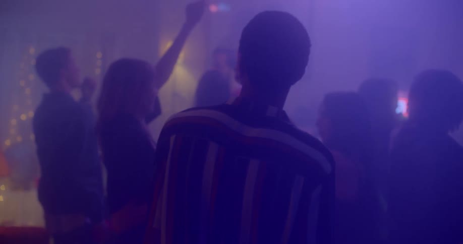 A man walks into a party where people are drinking and dancing and looks around
