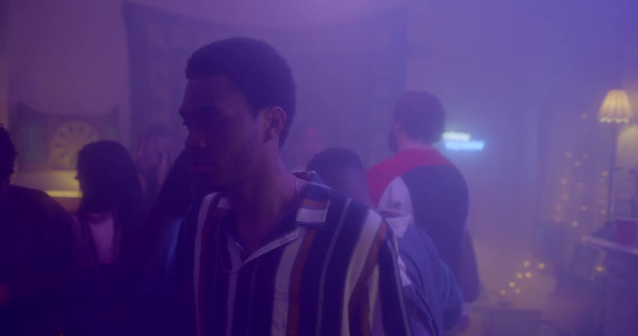 A young black male is walking through a crowded room during a house party