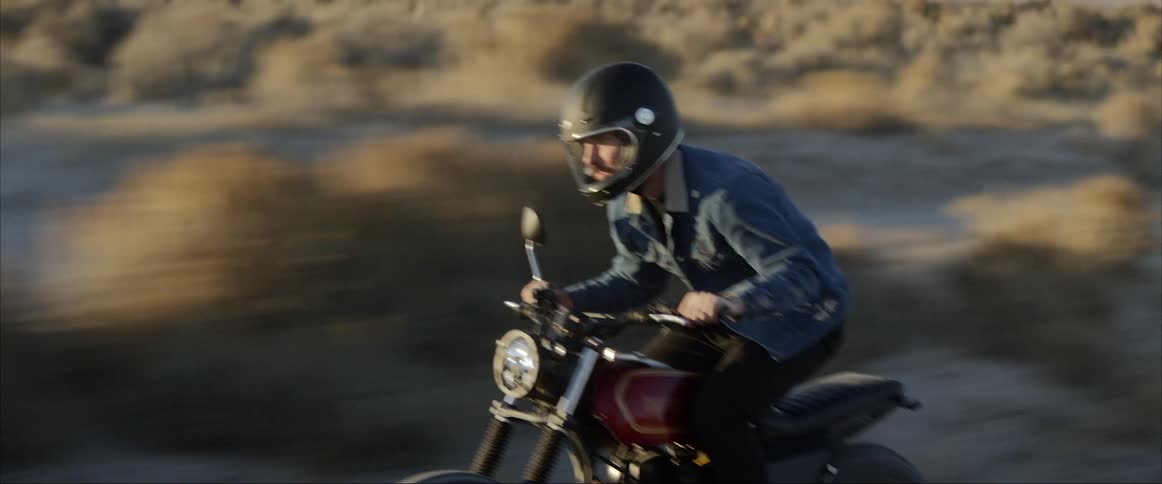Man rides motorcycle quickly past scrub covered plain