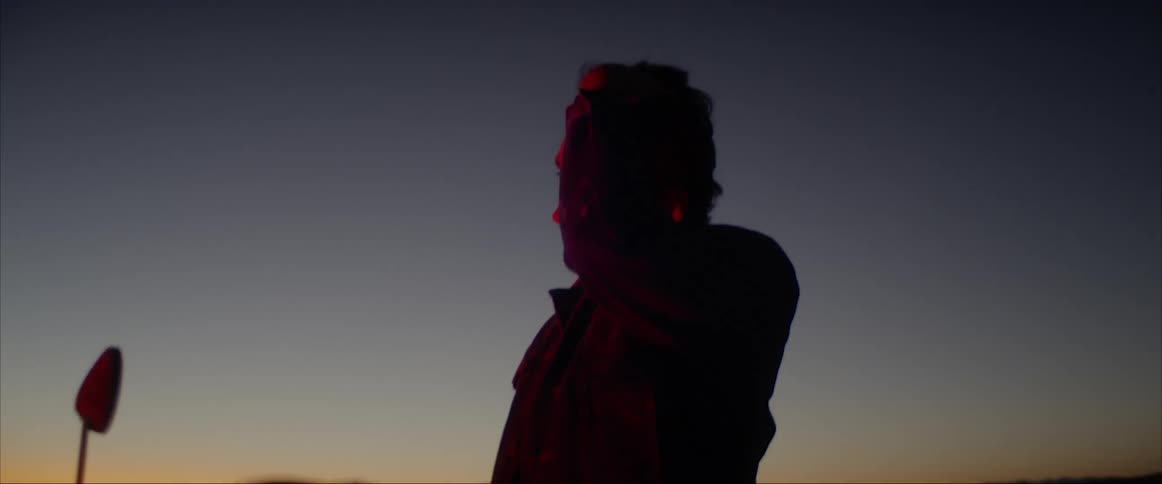 A man on a motorcycle in the desert taking off his helmet