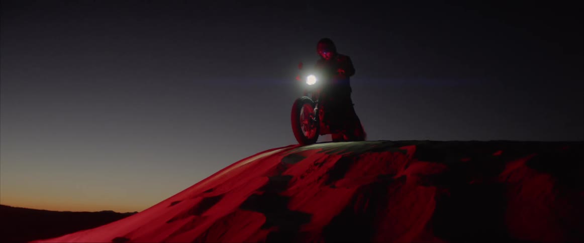 A man rides down a sandy hill on his motorcycle at night