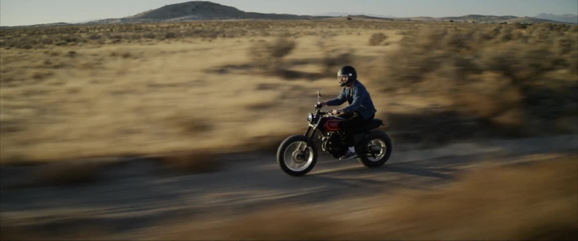 A man rides a motorcycle on a dirt road through the desert