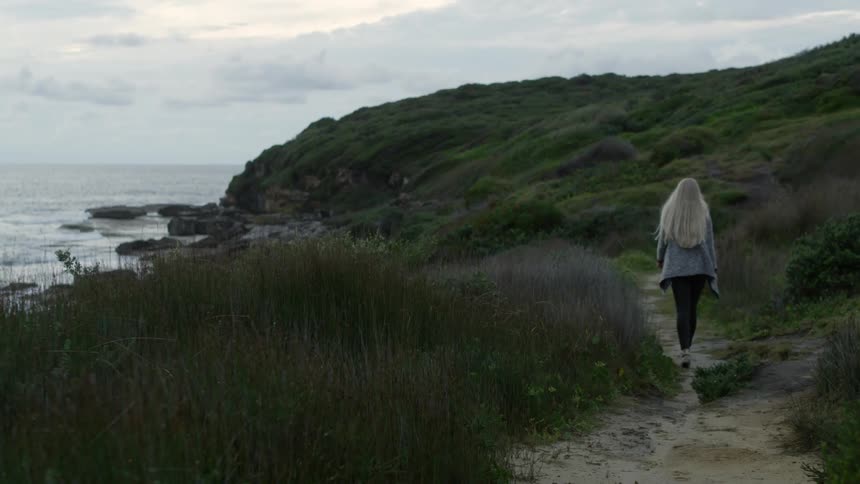 A woman walks on a path along the coast