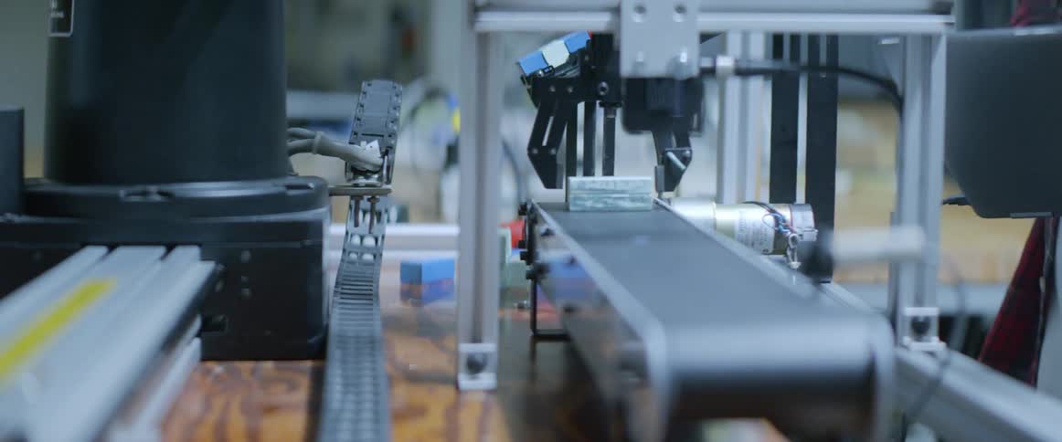 A robotic arm puts a chunk of metal on a conveyor belt
