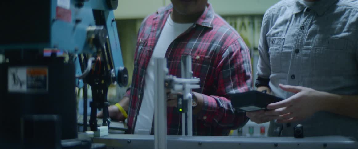 Two men talk with each other while standing in front of a piece of electronic equipment