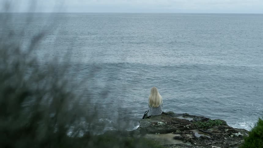 A woman sits on the edge of the water watching the tide come in