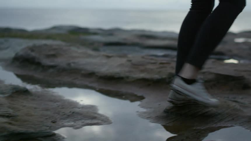 A person walks across puddles on a rock