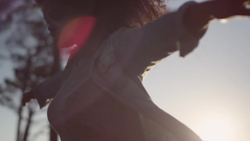 A woman balancing on something below camera is backlit by the sun