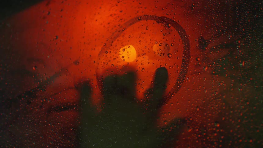 Someone drawing a smiley face on a window illuminated in red