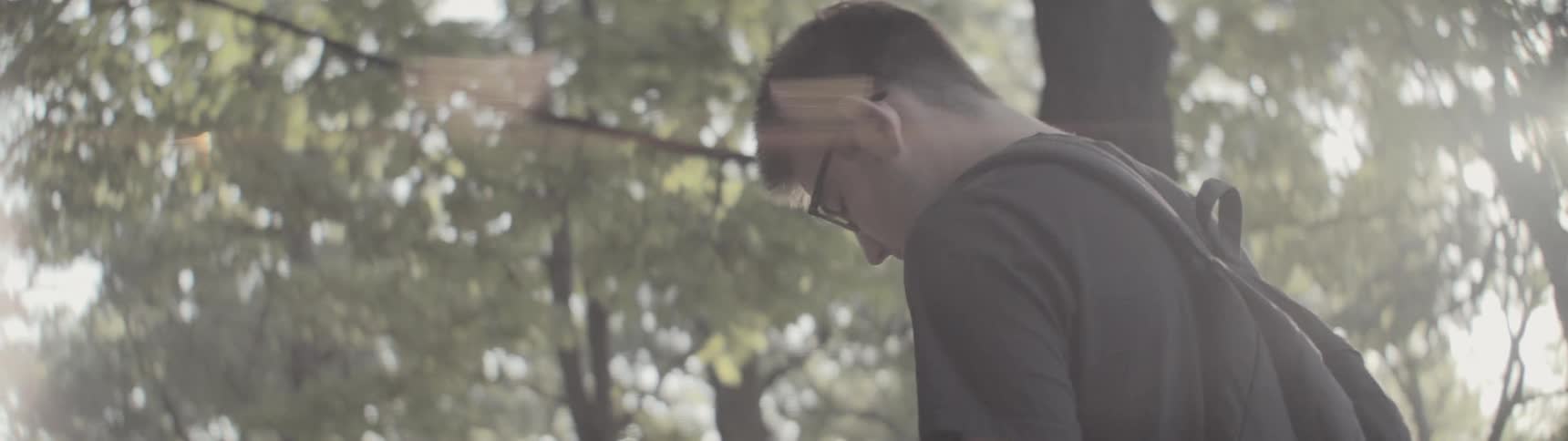 Man wearing backpack walks through trees during the day