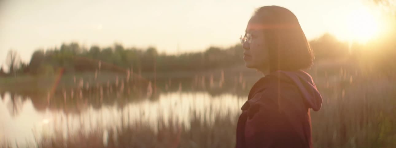Asian woman standing looking out to the lake against the sunlight