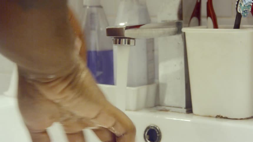 Males with a tattoo on his arm washes his hands off under the faucet in the bathroom