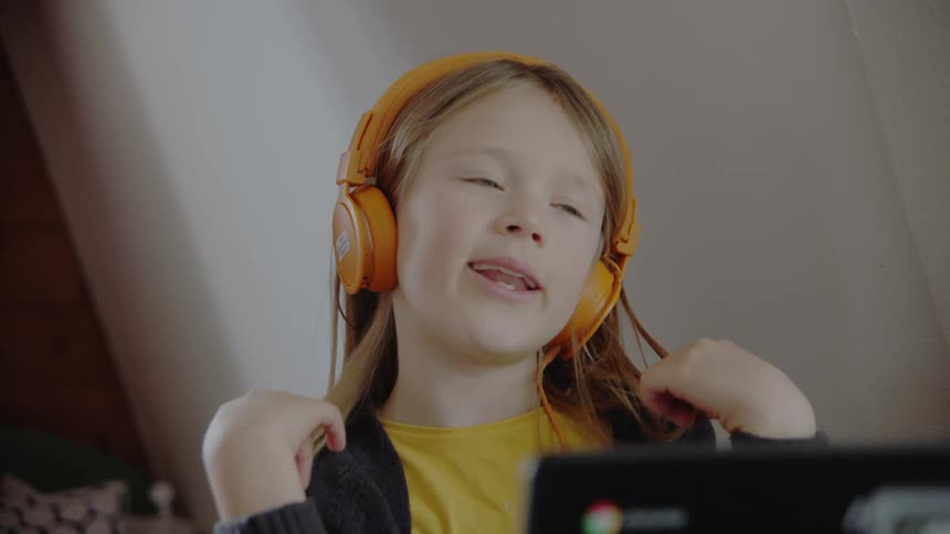 A little white girl speaks while wearing headphones