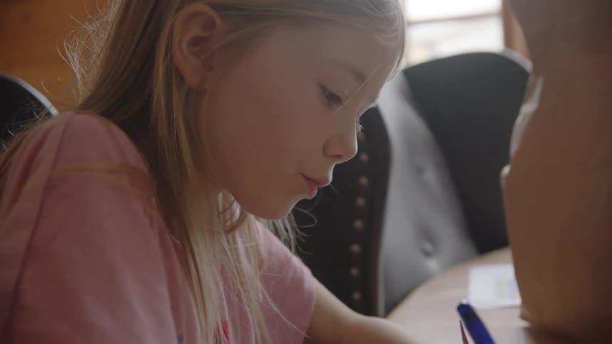 Girl sits at table drawing on paper