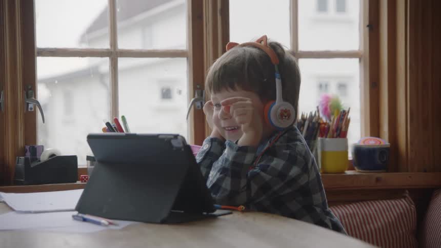 Little boy wearing headphones playing on his ipad at the table
