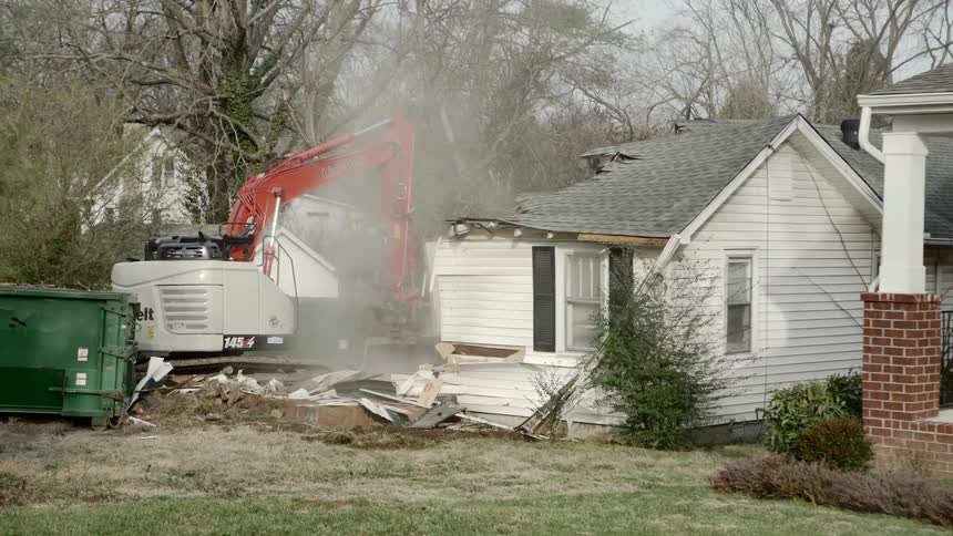 An excavator tears down a small white house