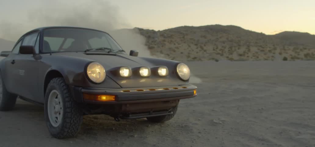 A car slowly driving to smoke in the middle of a desert