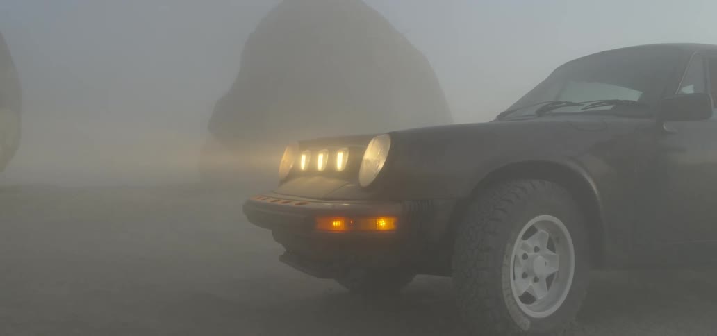 Car with headlights on parked outdoors near boulders on the fog