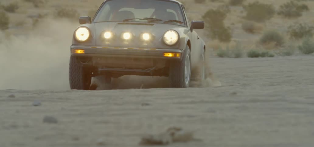 Man drives sports car rapidly across bare ground kicking up dust