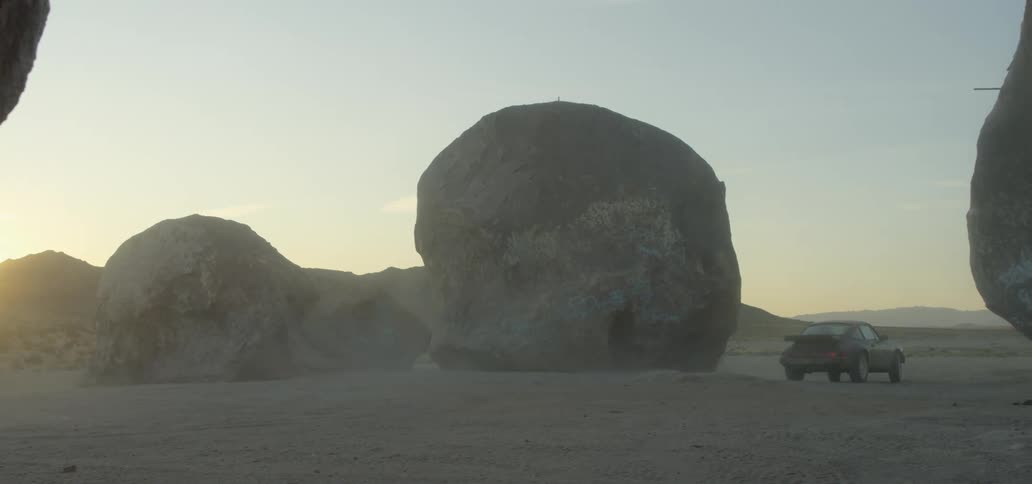 Car driving through large boulders at sunset