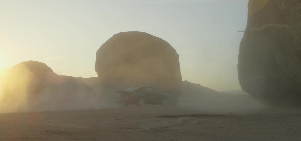 A sports car drives across a sandy area