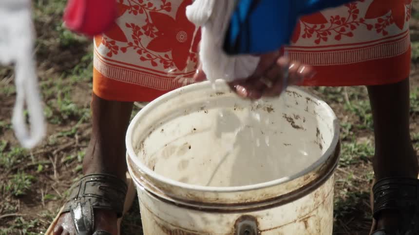 People are washing clothes inside of a bucket