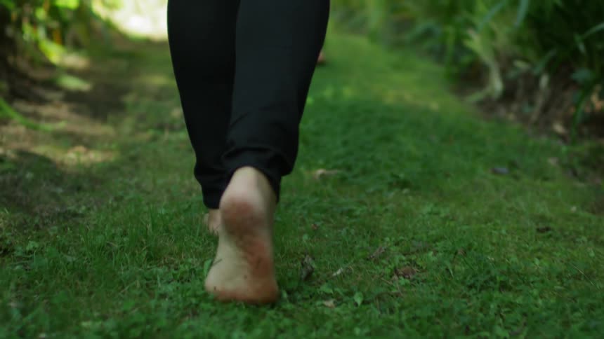 Two barefoot woman walk through greenery outside