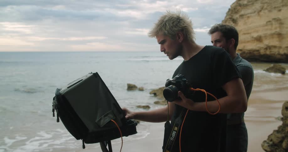 A photographer looks at a monitor set up on the shore of the beach