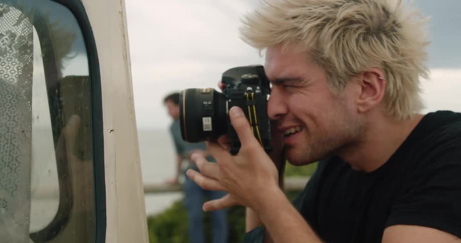 A man holds a camera to his face and aims it at a vehicle outside