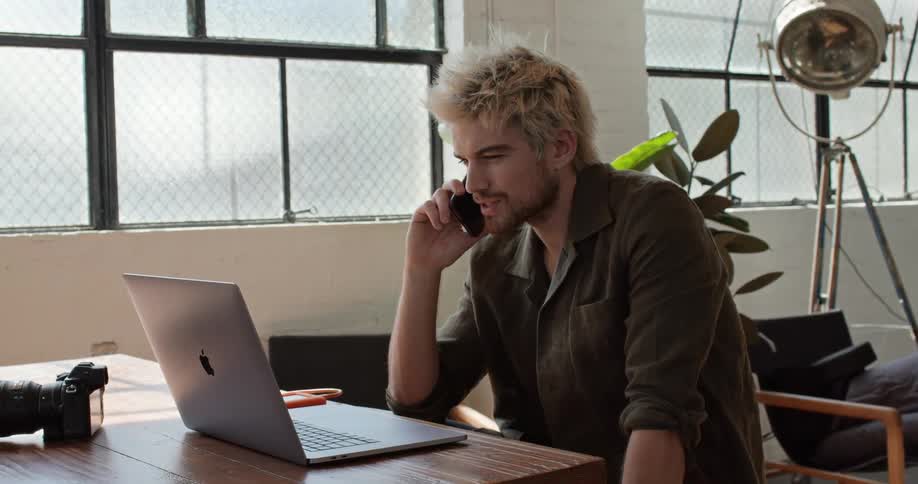 A man sitting at a desk looking at his laptop talking on the phone
