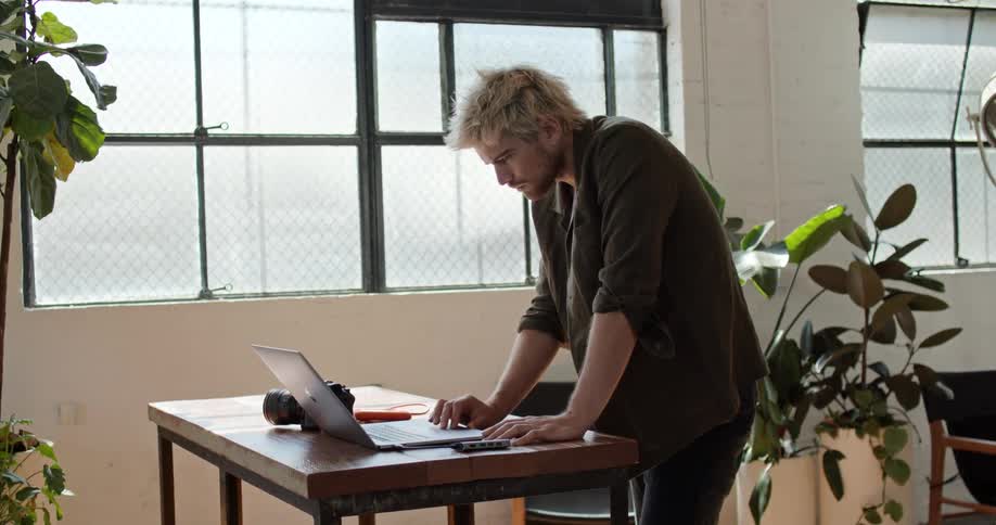 A man standing before a desk using a laptop