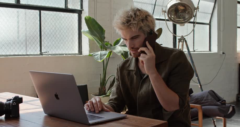 A man talks on his cellphone while using a laptop