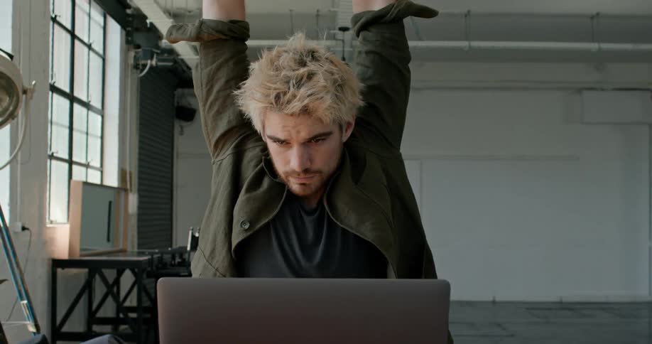 A man cracks his knuckles and stretches his arms while working on his laptop