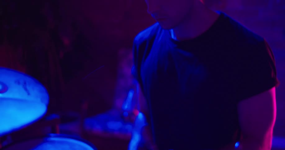 Person picks up drumsticks and begins drumming under blue light