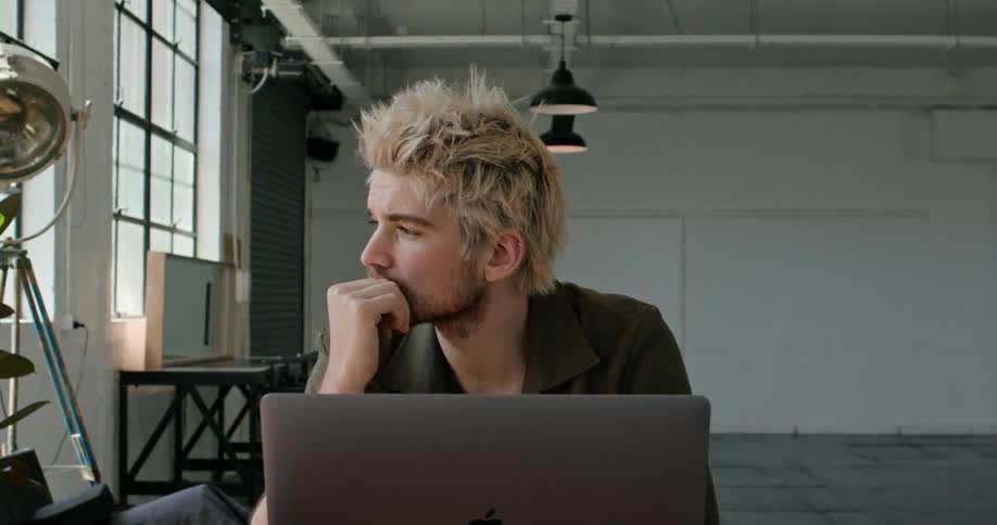 A man lost in thought while sitting before a laptop in a studio