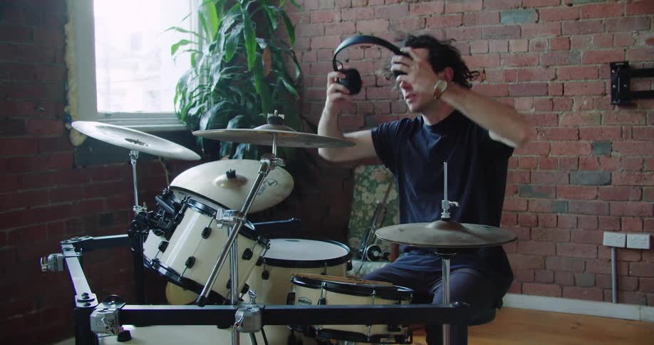 A man sits down at his drum set and puts on headphones