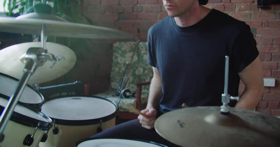 A young male with curly hair vigorously plays the drums