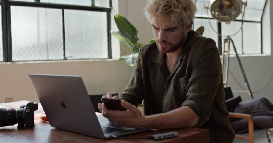 A man stops working on his laptop to look at his phone