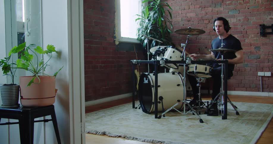 Man wears headphones while playing drums in residential room